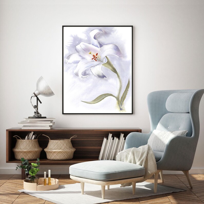May include: A framed watercolor painting of a white lily with a green stem and leaf. The artwork is displayed in a living room setting, with a light blue armchair, ottoman, and wooden cabinet.
