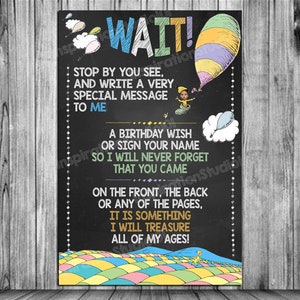 May include: A black chalkboard sign with colorful illustrations of a hot air balloon and a whimsical landscape. The sign reads "WAIT! Stop by you see, and write a very special message to me. A birthday wish or sign your name so I will never forget that you came. On the front, the back or any of the pages, it is something I will treasure all of my ages!"