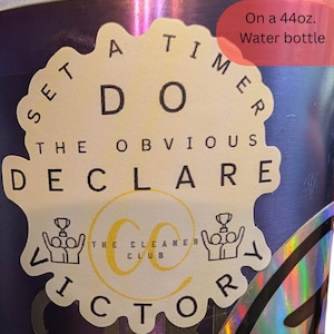 May include: A 44oz. water bottle featuring a scalloped-edge sticker with the text: SET A TIMER, DO THE OBVIOUS, DECLARE VICTORY, and THE CLEANER CLUB with a yellow CC logo and two figures holding trophies. The bottle has a dark blue metallic finish.