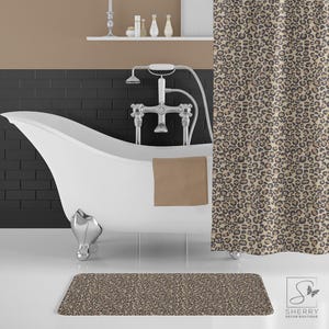 May include: A white bathtub with a brown towel and a shower curtain with a leopard print pattern. The shower curtain is beige with brown spots. The bathtub is in a bathroom with black tile walls.