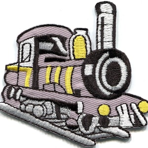 May include: An embroidered iron-on patch shaped like a steam locomotive train. The design features a light purple body with black outlines, white detailing on the wheels and smokestack, and bright yellow accents on the side and front lights.