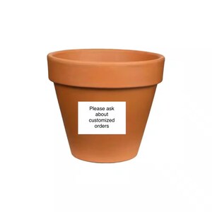 May include: A terracotta-colored flower pot with a wide rim and a tapered body. A white sticker on the front of the pot reads "Please ask about customized orders."