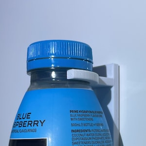 Pode incluir: Uma garrafa de plástico azul de bebida desportiva Prime Hydration sabor a framboesa azul com uma tampa branca e um rótulo branco com informações nutricionais. A garrafa é de 500 ml e contém adoçantes.