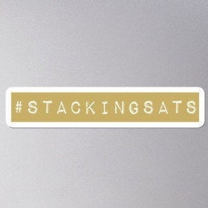 Puede incluir: Una pegatina dorada con el texto "#STACKINGSATS" en blanco.