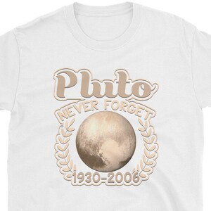May include: White t-shirt with a brown graphic of Pluto, a planet with a ring of leaves around it. The text "Pluto Never Forget 1930-2006" is printed on the shirt.
