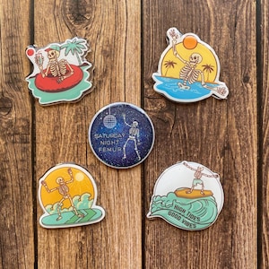 Peut inclure: Cinq épingles en émail colorées représentant un squelette dans diverses activités estivales. Les épingles comprennent un squelette dans un flotteur de piscine, un squelette faisant du surf, un squelette sur une planche de surf avec le texte "High Tides Good Vibes", un squelette sur une planche de surf avec un coucher de soleil derrière lui, et un squelette dansant avec un ballon disco sur fond de galaxie avec le texte "Saturday Night Fever".