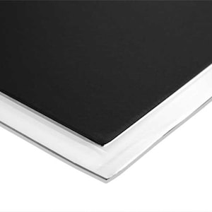 Op de afbeelding: Close-up van de rand van een zwart notitieboek met witte pagina's. Het notitieboek heeft een glad, zwart omslag en een witte rug.