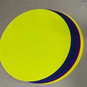 May include: Four round, flat discs stacked on top of each other. The top disc is yellow, the next is blue, the next is black, and the bottom disc is red.