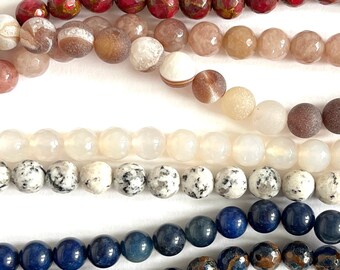 May include: Assortment of gemstone beads in various colours and patterns, including red, brown, white, and blue. The beads are arranged in rows, with the top row being red, the second row being brown and white, the third row being white, and the bottom row being blue.
