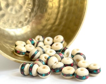 May include: A bowl of white bone beads with red and turquoise geometric patterns. The beads are round and have a smooth finish.