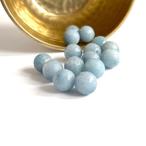 May include: A group of light blue round beads, scattered on a white surface. The beads are smooth and glossy, and they appear to be made of natural stone.