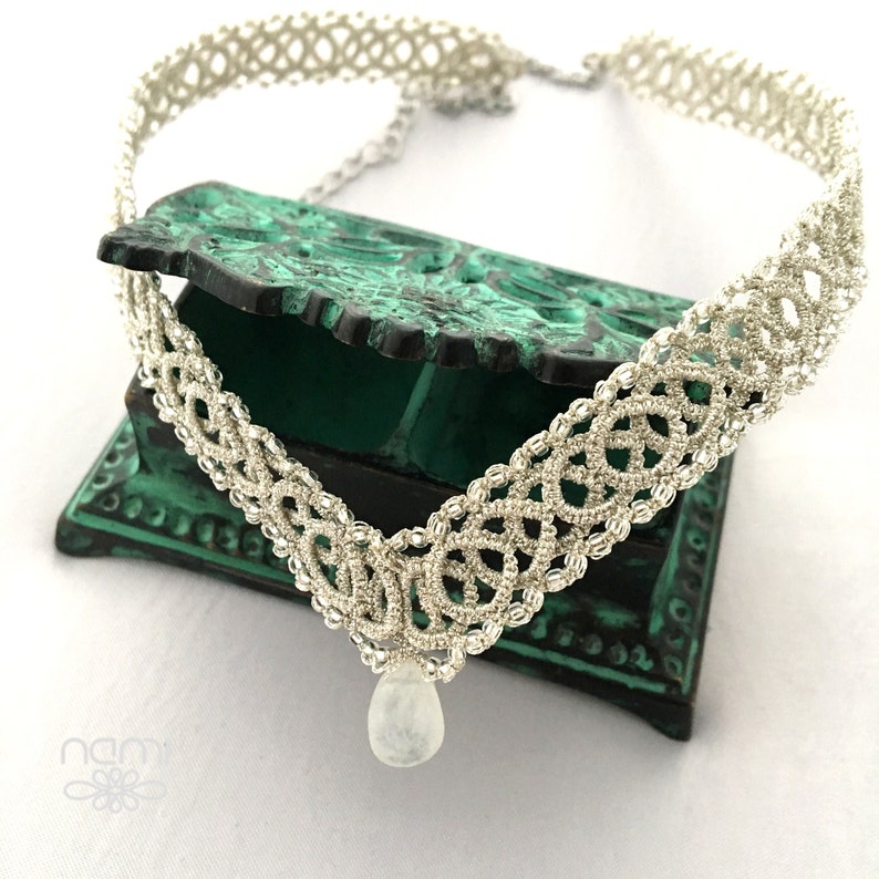 May include: A silver crocheted choker necklace with a teardrop-shaped moonstone pendant.