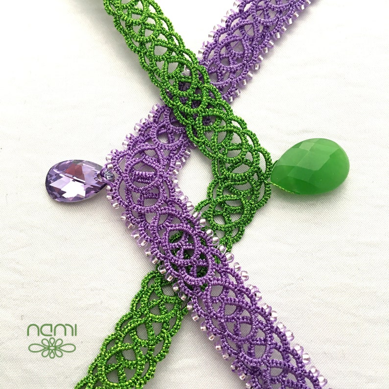 May include: Two handmade crocheted necklaces with a green and purple design. The necklaces are adorned with a green and a purple teardrop-shaped pendant.
