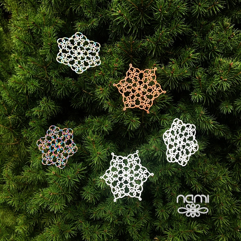 May include: Five white crocheted snowflakes with different designs, including one with iridescent thread, on a green evergreen tree background.