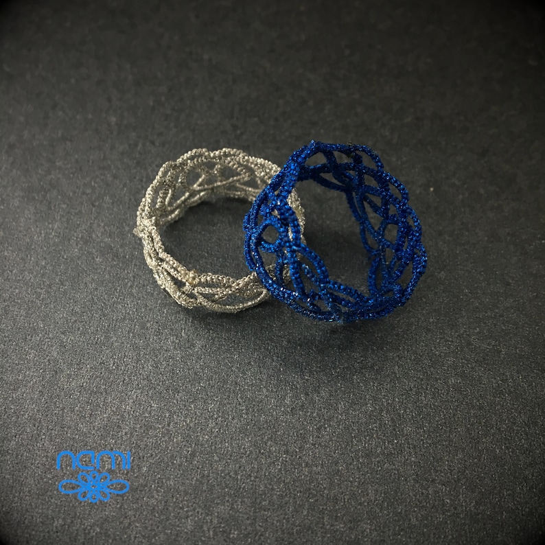 May include: Two crocheted rings, one silver and one blue, are stacked on top of each other. The rings are made of a delicate, intricate pattern.