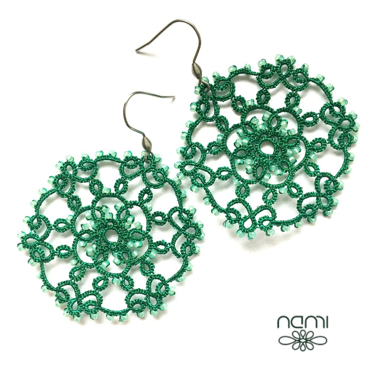 May include: A pair of green crocheted earrings with silver hooks. The earrings are round and feature a delicate, intricate design.