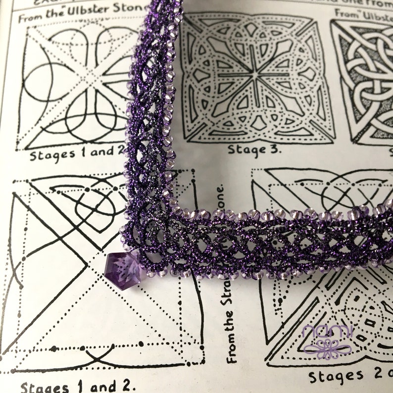 May include: A close-up of a purple beaded lace trim with a silver thread running through it. The trim is laid on top of a page from a book with black and white line drawings of geometric patterns. The text on the page reads "From the Ulbster Stone" and "Stages 1 and 2".