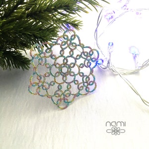 May include: A multi-colored iridescent snowflake ornament with a delicate, intricate design. The snowflake is made of wire and is hanging from a string of white Christmas lights.