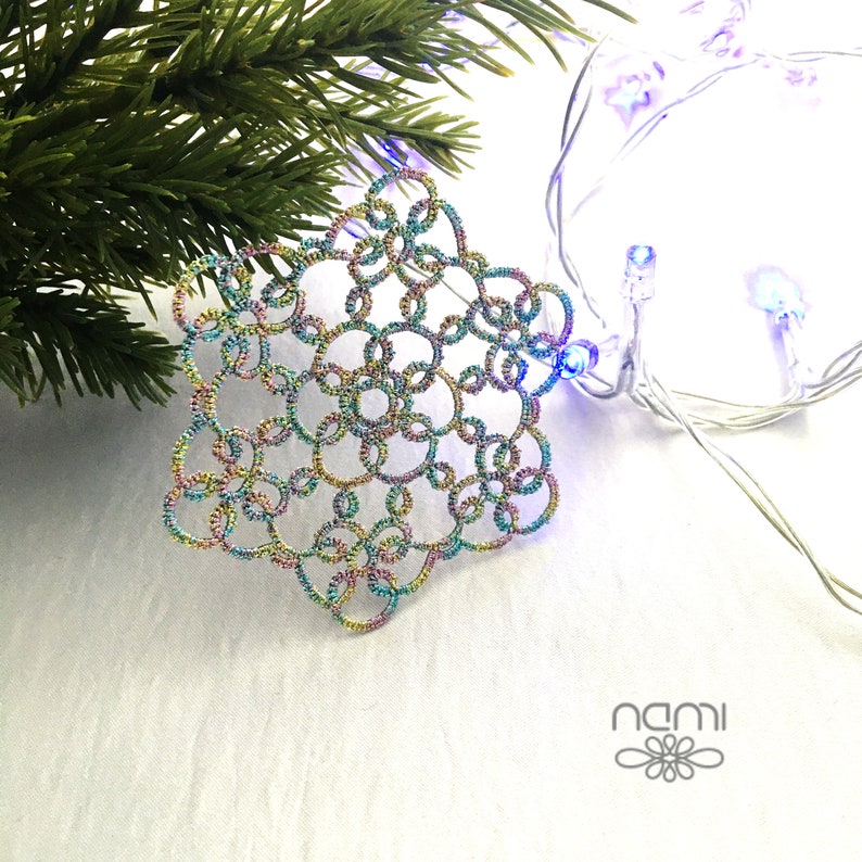 May include: A multi-colored iridescent snowflake ornament with a delicate, intricate design. The snowflake is made of wire and is hanging from a string of white Christmas lights.