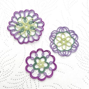 K&ouml;nnte beinhalten: Drei handgefertigte, kreisf&ouml;rmige Spitzendeckchen in Lila, Gr&uuml;n und Gelb. Jedes Deckchen hat ein Blumendesign mit aufwendigen Details. Die Deckchen sind auf einer wei&szlig;en, strukturierten Oberfl&auml;che angeordnet.