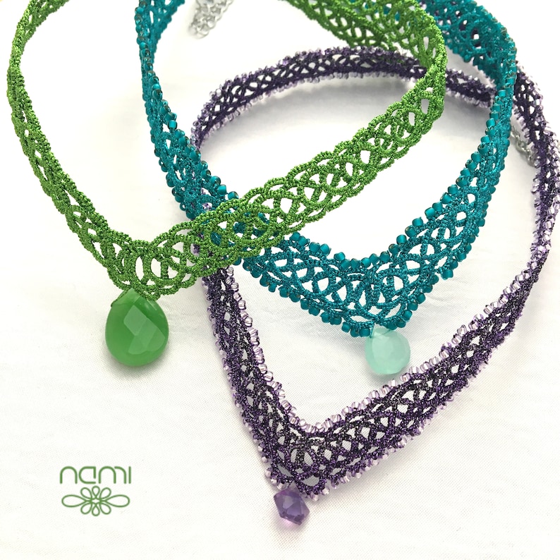 May include: Three crocheted necklaces with green, teal, and purple beads. The necklaces are layered on top of each other and have a teardrop-shaped pendant on each.