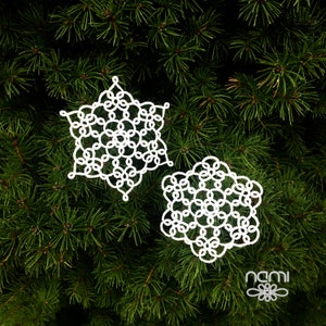 May include: Two white crocheted snowflakes on a green pine tree background.