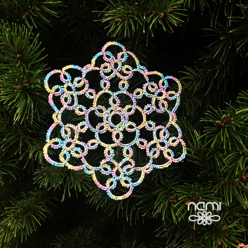 May include: A colorful snowflake ornament made of delicate crocheted thread. The snowflake is a light blue, pink, and yellow color and has a sparkly finish.