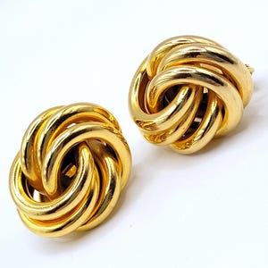 May include: A pair of gold knot-shaped earrings. The earrings are made of a thick, twisted gold wire.