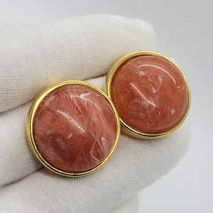 May include: A pair of gold tone clip-on earrings with a pink and white marbled design.