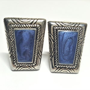 Puede incluir: Un par de pendientes de tono plateado con un rectángulo de esmalte azul en el centro. El rectángulo está rodeado por un marco plateado con un diseño de cuerda. Los pendientes tienen un diseño texturizado alrededor del exterior.