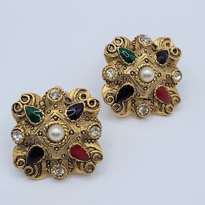 以下が含まれることがあります： 正方形のデザインのゴールドトーンのイヤリングのペア。イヤリングは、赤、緑、黒の石、クリアなラインストーン、そして中央にパールで飾られています。