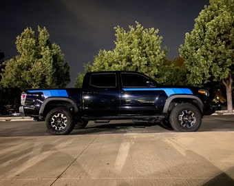 Puede incluir: Una camioneta negra con rayas de carreras azules y negras a los lados. La camioneta está estacionada en un estacionamiento por la noche.