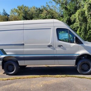 May include: A white van with a blue and gray stripe along the side. The van has black wheels and a black bumper.