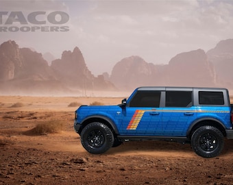May include: A blue Ford Bronco with a "Taco Troopers" decal on the side. The car is in a desert setting with mountains in the background.