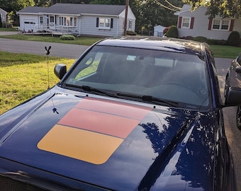 Puede incluir: Una camioneta pick-up azul oscuro con una franja de carreras naranja y roja personalizada en el capó. La camioneta tiene una parrilla negra y una antena negra.