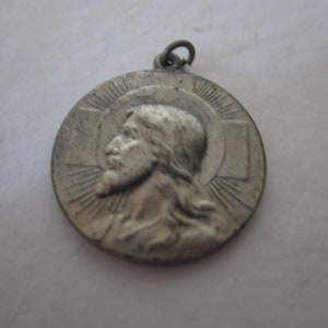 May include: Silver pendant featuring a profile of Jesus Christ with a halo and a cross behind him.