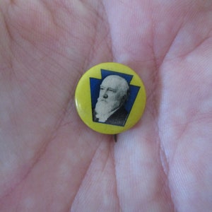 May include: A yellow button with a blue outline of the state of Pennsylvania and a black and white image of a man's face.