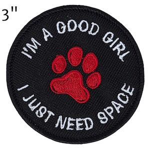 May include: A round, black embroidered patch with white text that reads "I'M A GOOD GIRL I JUST NEED SPACE." A red paw print is in the center. The patch is 3 inches in diameter.