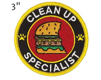 May include: Embroidered patch, 7.6 cm in diameter, with a yellow border and the words "CLEAN UP SPECIALIST" in white. The patch features a red center with a cartoon burger and paw prints.