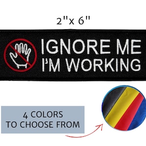 May include: Black embroidered patch, 2" x 6", with white text reading "IGNORE ME I'M WORKING". A red circle with a line through a hand graphic is on the left. Includes a color selection graphic with four color options.