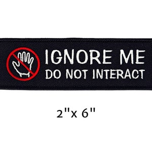May include: Black rectangular patch with white text that reads "IGNORE ME DO NOT INTERACT". A red circle with a hand inside and a red line through it is on the left. The patch measures 2" x 6".