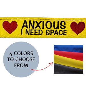 May include: A yellow dog collar attachment with the text "ANXIOUS I NEED SPACE" and two red hearts. The attachment is shown with a red and black paw print leash. The image also shows a color chart with four color options.