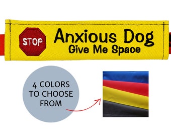 May include: Yellow fabric dog collar attachment with the text "Anxious Dog Give Me Space". Includes a red "STOP" sign and a paw print design. The image also shows four color options: blue, red, yellow, and black.