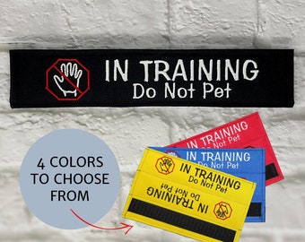 May include: Black, red, blue, and yellow patches with the text "IN TRAINING Do Not Pet". Each patch features a hand symbol inside a red stop sign. The image also includes the text "4 COLORS TO CHOOSE FROM".