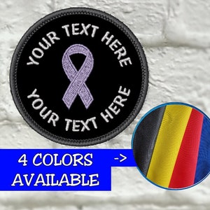 May include: A round black patch with embroidered text "YOUR TEXT HERE" and a purple ribbon in the center. The patch has a black border and a small inset showing four fabric colors. The text "4 COLORS AVAILABLE" is in a blue rectangle.
