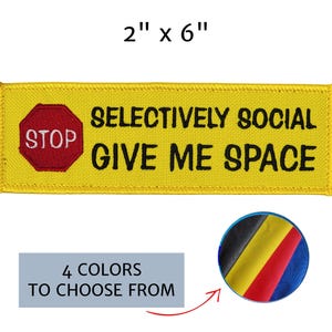 May include: A rectangular yellow embroidered patch measuring 2 inches by 6 inches. It features a red stop sign icon on the left and the black text SELECTIVELY SOCIAL GIVE ME SPACE. A circular inset shows four fabric color options: black, yellow, red, and blue.