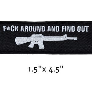 May include: Black rectangular patch with white embroidered text and a rifle graphic. The text reads "F*CK AROUND AND FIND OUT." The patch measures 1.5" x 4.5".