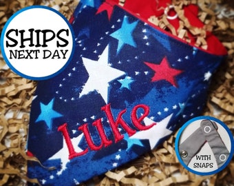 May include: A reversible dog bandana with a patriotic theme. The blue fabric is decorated with white, red, and blue stars. The name "Luke" is embroidered in red. The bandana has snaps for easy closure.