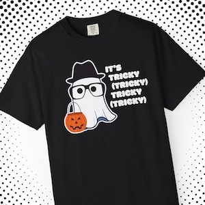 May include: Black t-shirt featuring a cartoon ghost wearing a hat and glasses, holding an orange jack-o'-lantern. The text on the shirt reads "It's Tricky (Tricky) Tricky (Tricky)".