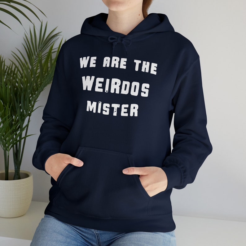 May include: A navy blue hooded sweatshirt featuring a front kangaroo pocket and long sleeves. The chest displays the white, distressed-style text "WE ARE THE WEIRDOS MISTER" in a bold, sans-serif font. The garment includes a matching drawstring hood.